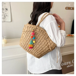 Detail of bohemian straw woven tote bag featuring colorful tassels and pom poms