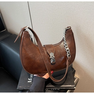 Detail of dark brown crescent bag featuring polished PU leather and silver metal clasp