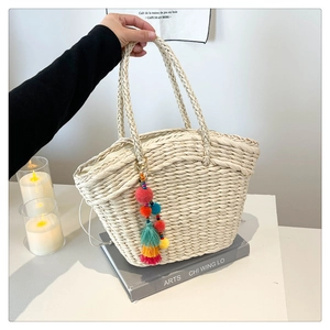 Close-up of beige woven straw tote bag featuring a colorful pom-pom tassel charm detail