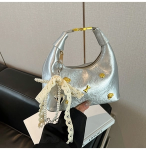 Detail of silver metallic hobo bag with lace bow, pearl chain and gold charms