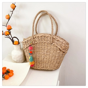 Detail of hand-woven straw basket bag featuring colorful pompom tassels and textured weave