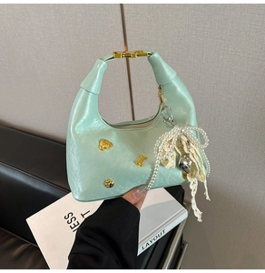 Detail of mint green matte bag featuring golden dog charms and pearl lace bow accessory