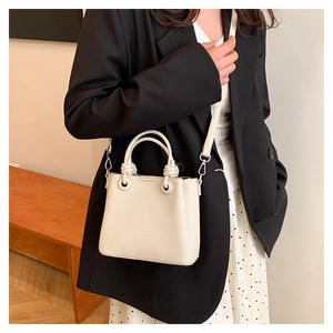 Chic beige lychee leather handbag with knot handle detail shown on model in black suit