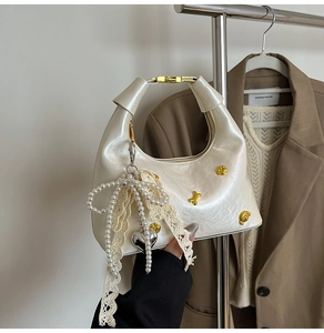 Detail of cream pearlescent leather bag with gold hardware and pearl ribbon charm