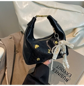 Detail of black pleated dumpling bag with pearl bow and golden metal charms