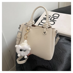 Detail of off-white lychee grain leather bag featuring a cute plush monster pendant