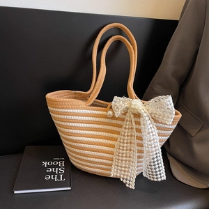 Striped woven beach tote with lace bow and pearl detail on a dark scene background