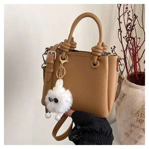 Brown litchi grain leather handbag featuring a white plush monster charm and top handle