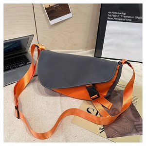 Close-up of contrast crossbody bag with grey flap and orange base on a woven surface