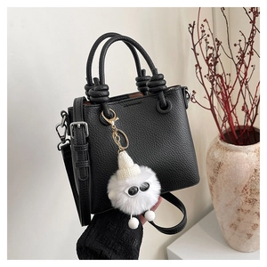 Detail of black lychee leather handbag with knot handles and plush monster charm
