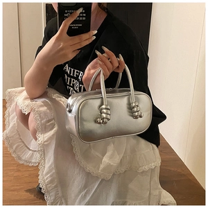 Détail du sac argenté métallisé avec poignée à nœud sphérique et forme Boston ronde