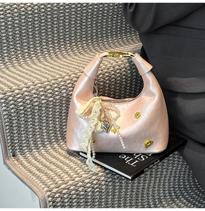 Detail of pink crescent bag with pearl chain, lace ribbon, and gold bear charm accent