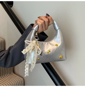 Close-up of silver dumpling bag with metallic studs, lace bow, and pearl chain detail
