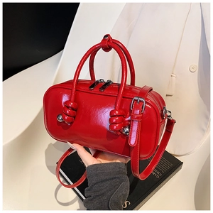 Détail du sac cylindrique en cuir verni rouge avec poignée nouée et finitions argentées