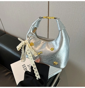 Detailed shot of silver dumpling bag with lace pearl bow and gold embossed metallic charms