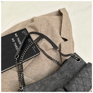 Detailed view of dark grey quilted shoulder bag with chain strap on a herringbone blazer