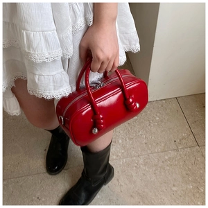 Détail du sac cylindrique rouge brillant avec poignées nouées et détails métalliques