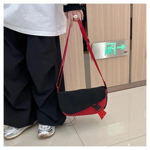 Close-up of black and red messenger bag with buckle closure and red strap on model