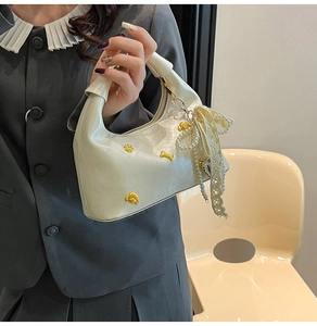 Close-up of creamy dumpling bag with golden puppy charms and pearl lace bow detail