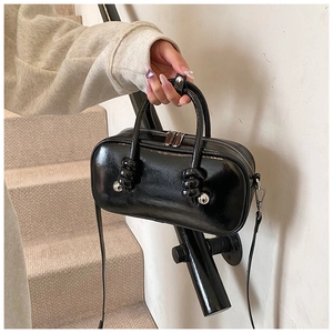 Détail du sac bandoulière en cuir verni noir avec poignée nouée et finitions argent
