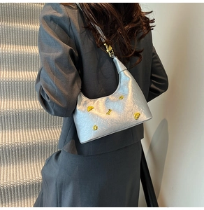Close-up of silver pleated crossbody bag with decorative gold dog charms on model