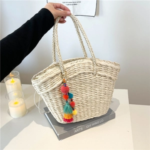 Handcrafted cream woven straw basket bag with colorful pom-poms for beach vacation style