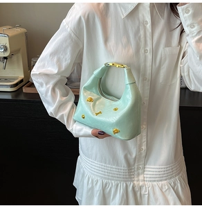 Detail of mint green hobo bag with golden bear studs held by model in white shirt