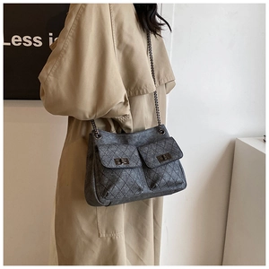 Detail of dark grey quilted chain bag with dual flap pockets shown on a beige trench coat