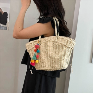Beige woven straw tote bag with bohemian tassels and drawstring closure for beach