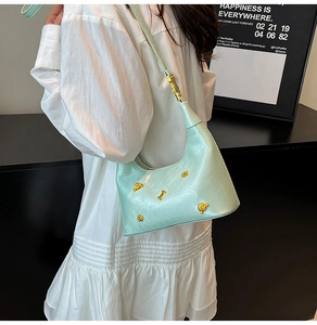 Detail of mint green dumpling bag with gold bone and paw charms on leather strap