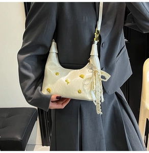 Detail of cream crescent bag featuring gold stud accents and a pearl lace bow charm