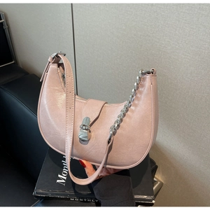 Sac hobo rose avec boucle argentée, lanières en cuir et chaîne présentées sur un livre