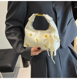 Detail of cream glossy handbag with golden floral accents and pearl charm strap