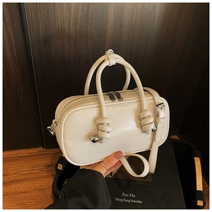 Détail du sac cylindrique blanc cassé avec poignée nouée unique et ornements de boules en métal