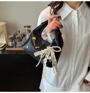 Detail of crescent shoulder bag featuring gold charms, lace bow, and pearl chain accents