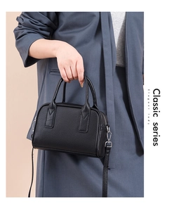 Close-up of a black pebbled leather bowling bag held by a model in a grey suit