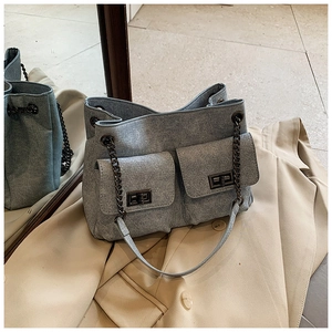 Detail of grey denim bag with quilted pockets and metal chain on beige blazer