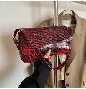 Détail du sac baguette rouge à motif serpent avec bandoulière et boucles dorées