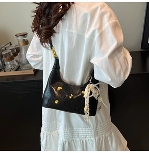 Detail of black Hobo bag with pearl charms, lace bow, and yellow flower accents on model