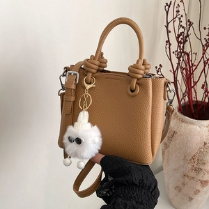 Brown lychee leather tote bag with monster charm and knotted handle on neutral background