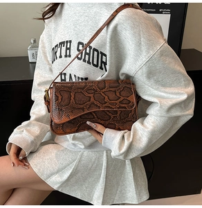 Détail du sac bandoulière marron en serpent sur sweat gris avec rabat élégant et texture