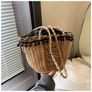 Detailed close-up of woven straw bag with black pom-pom trim and drawstring lining