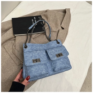 Macro detail of blue denim shoulder bag featuring quilted stitching and metal turn-lock pockets