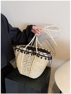 Detail of woven straw bucket bag with black pompom trim and braided rope handle