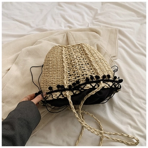Top view of handmade straw bucket bag with black pom-poms and drawstring closure