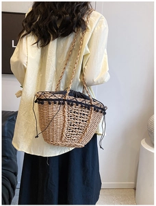 Detail of straw woven shoulder bag featuring black pom-pom trim and drawstring lining