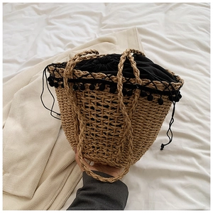 Detail of straw woven bucket bag featuring black drawstring closure and pom-pom trim accents
