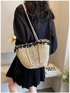 Detail of straw tote bag featuring diamond weave pattern and black pom-pom trim accents