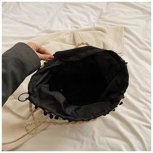Detail view of woven straw tote bag with black pompom trim and spacious inner lining