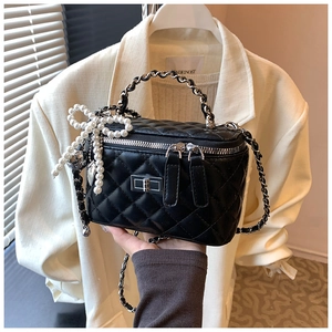 Detail of black quilted leather vanity bag with pearl bow charm and chain handle